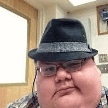 a man wearing a fedora hat and glasses is taking a selfie .