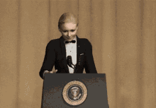 a woman in a tuxedo stands behind a podium with the seal of the president of the united states on it