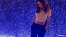 a woman in a white crop top and black pants is standing in front of a wall with blue lights .