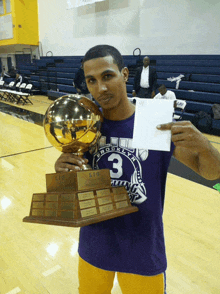 a man in a purple shirt with the number 3 holding a trophy