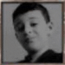 a black and white photo of a young boy looking at the camera .