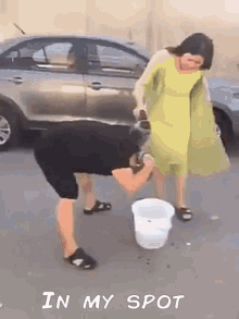 a woman in a yellow dress is standing next to a man with a bucket of water in front of a car .