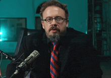 a man with glasses and a beard is sitting in front of a microphone