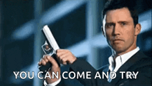 a man in a suit is holding a gun in his hand and says `` you can come and try '' .