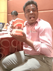 a man in a pink shirt holds a model of teeth in his hand