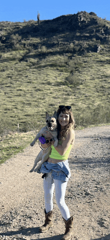 a woman is holding a dog on a dirt path