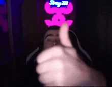 a man is giving a thumbs up in front of a pink neon sign .