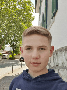 a young boy wearing a blue hoodie stands in front of a white building and trees