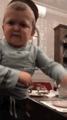 a baby in a blue shirt is standing in front of a table with plates and a coca cola bottle on it