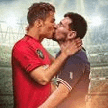 two men are kissing each other on a soccer field in front of a crowd .