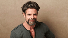 a man with a beard is smiling for the camera while wearing a gray shirt .