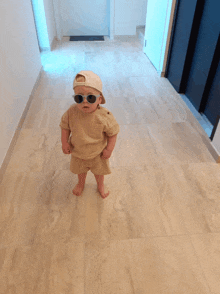 a baby wearing sunglasses and a baseball cap is standing on a tiled floor