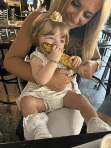 a woman is holding a baby who is eating a corn on the cob