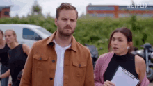 a man and a woman are standing next to each other in a parking lot . the man is holding a clipboard .