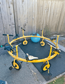 a circle of yellow tricycles sits on a mat outside