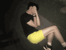 a man wearing yellow shorts and a black shirt is covering his face with his hands