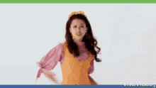 a woman in a pink shirt and orange vest is dancing in front of a green background .