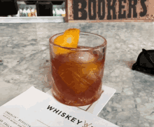 a glass of whiskey sits on a napkin next to a menu for bookers