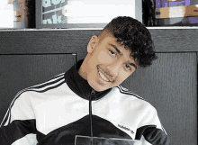 a young man wearing a black and white adidas jacket smiles for the camera