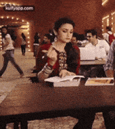 a woman is sitting at a table in a classroom with a book and a pen in her hand .