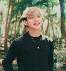 a young man with braces on his teeth is standing in the woods wearing a black shirt and necklace .