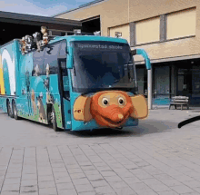 a blue bus with a cartoon elephant face on the front is parked in front of a building .