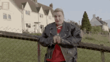 a woman in a leather jacket is standing next to a chain link fence in front of a house .