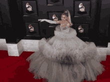 a woman in a ball gown stands on a red carpet in front of a wall with grammy awards on it