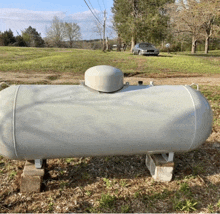 a large white propane tank is sitting on concrete blocks in a field