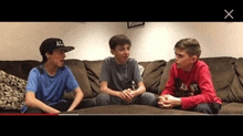 three boys are sitting on a couch talking to each other