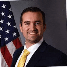 a man in a suit and tie is smiling in front of a flag .