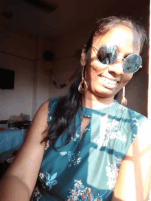 a woman wearing sunglasses and a floral shirt smiles for the camera