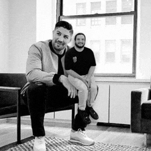 two men are sitting on chairs in front of a window .