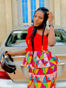 a woman in a colorful dress stands in front of a silver car