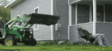 a man is laying in a chair in front of a house while a green tractor is parked in front of it .