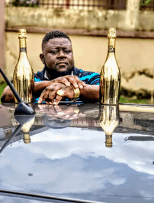 a man leans on a car with two gold bottles of champagne