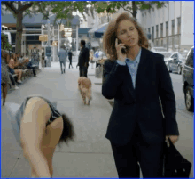 a woman in a suit is talking on a cell phone while walking down the street