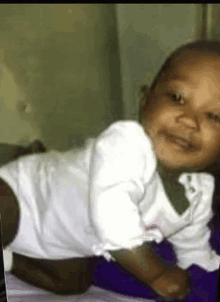 a baby in a white shirt is laying on its stomach on a bed and smiling .