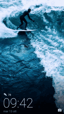 a phone screen shows a surfer in the ocean and the time is 9:42