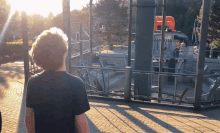 a boy in a black shirt stands in front of a rollercoaster