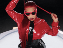 a woman wearing sunglasses and a red jacket holds a red whip