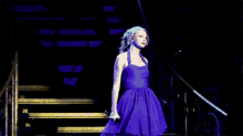 a woman in a blue dress is walking down stairs with a microphone in her hand