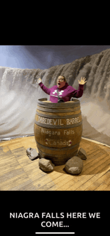 a woman is standing in a daredevil barrel in front of a waterfall