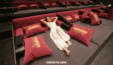 a woman in a white dress is laying on a couch with red pillows that say rude do cinema