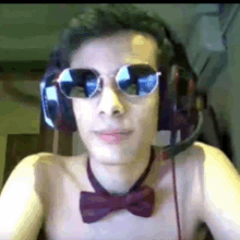 a shirtless man wearing headphones , sunglasses and a bow tie is looking at the camera .