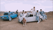 a group of young men are posing for a picture in front of a blue car and a white car