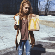 a woman is holding a mcdonald 's bag and a cup