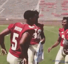 a group of football players are standing on a field . one of the players is wearing a number 5 jersey .