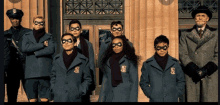 a group of people standing in front of a building wearing masks and jackets with the letter s on them