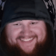 a man with a beard wearing headphones and a hat smiles for the camera